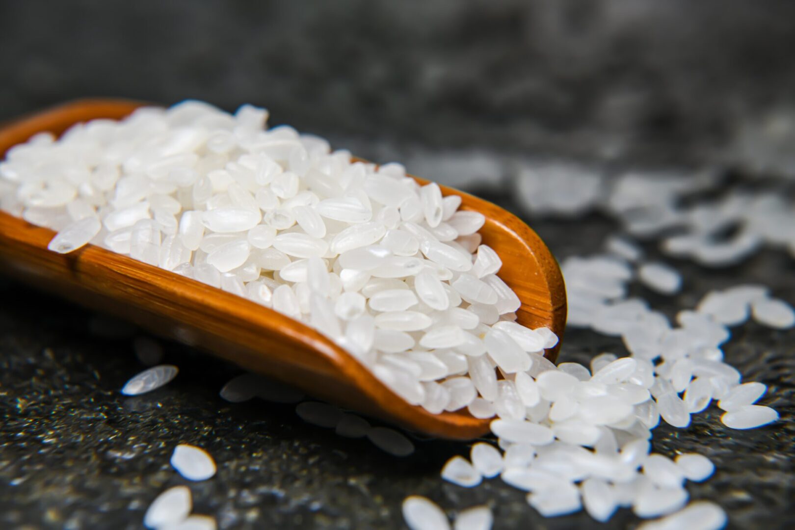 A wooden spoon filled with white rice on top of some rocks.