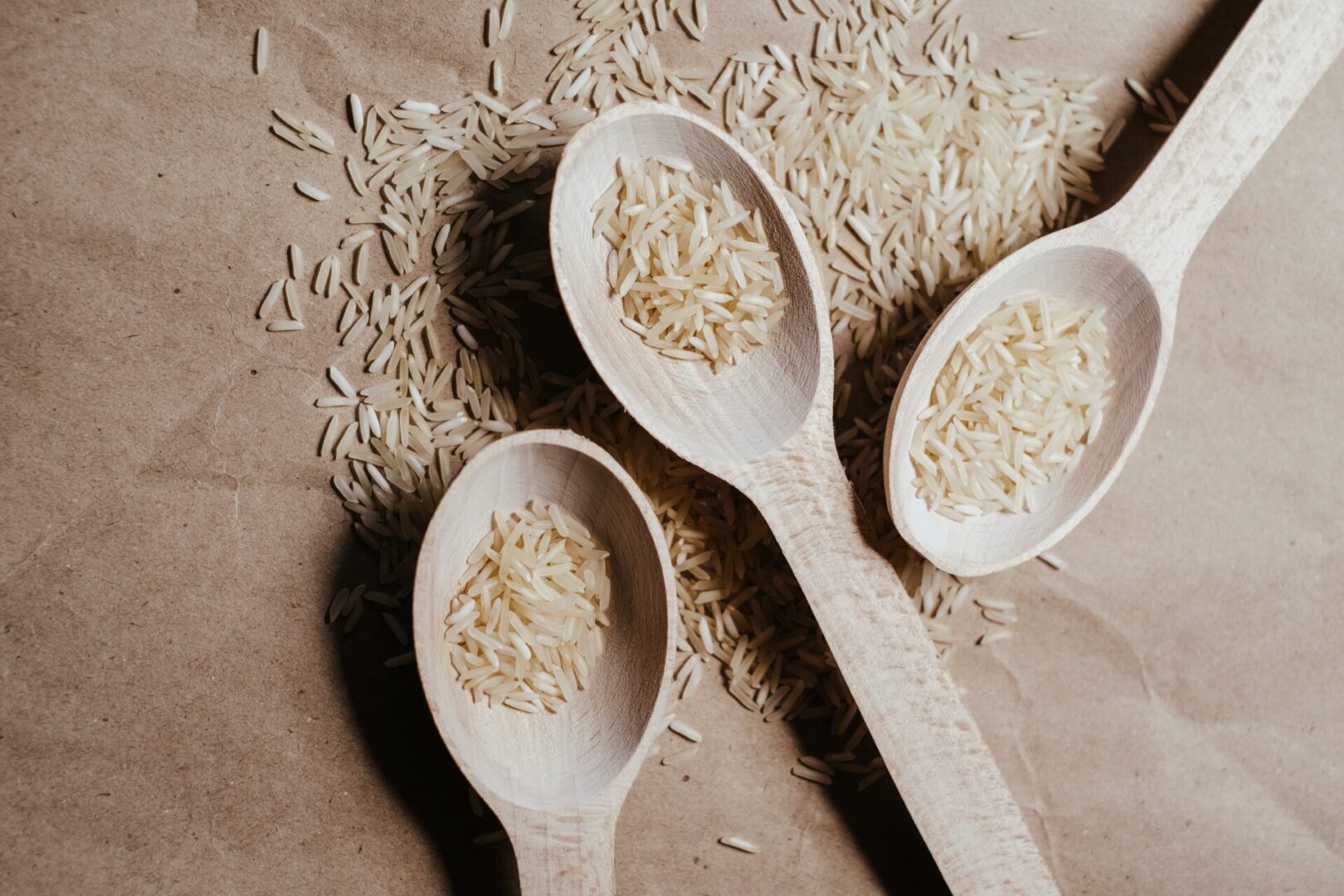 Three wooden spoons with rice on them sitting next to a pile of rice.